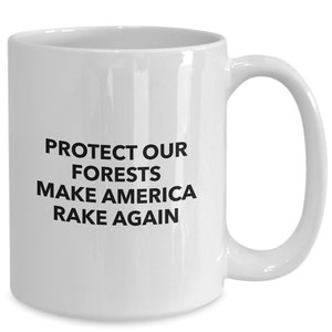 May include: White ceramic coffee mug with black text that reads "PROTECT OUR FORESTS MAKE AMERICA RAKE AGAIN".