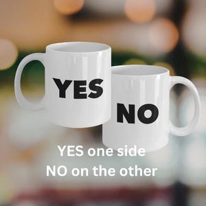 May include: Two white ceramic mugs. One mug has the word "YES" in bold black letters. The other mug has the word "NO" in bold black letters. Text below the mugs reads "YES one side NO on the other."