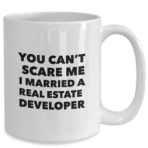 May include: White ceramic coffee mug with black text that reads "You can't scare me I married a real estate developer".