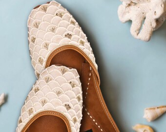 May include: A pair of white leather shoes with intricate beaded embellishments. The shoes have a brown leather lining and a label that reads "handicrafts in me".
