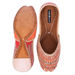 May include: A pair of orange and red embroidered flat shoes with gold embellishments. The shoes have a leather sole and are decorated with sequins and beads. The text "Handicrafts in me" is visible on the inside of one shoe.