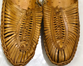 May include: A pair of tan leather sandals with a woven design. The sandals have a simple, slip-on style and are made of a soft, supple leather.