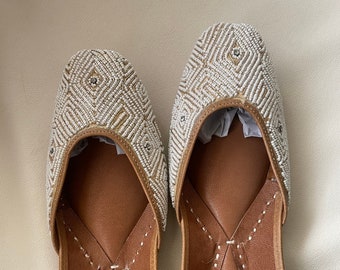 May include: A pair of white leather shoes with intricate beaded designs. The shoes have a brown leather lining and a pointed toe.