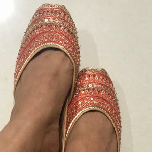 May include: A pair of orange and gold embroidered flat shoes with sequins.