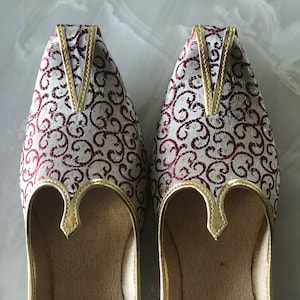 May include: A pair of white and burgundy embroidered shoes with gold trim. The shoes have a pointed toe and a closed back.