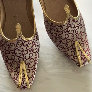 May include: A pair of gold and burgundy patterned shoes with pointed toes and gold trim. The shoes have a traditional design.