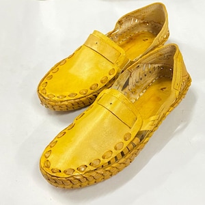 May include: A pair of yellow leather sandals with a woven design. The sandals have a closed toe and a strap across the top of the foot.