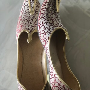 May include: A pair of white and burgundy patterned shoes with gold trim. The shoes have a pointed toe and a closed back.