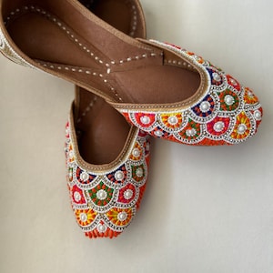 May include: A pair of flat, orange leather shoes with colorful embroidery and pearl accents.
