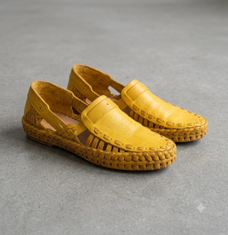 May include: A pair of mustard yellow leather loafers featuring a woven design along the sides and base. The shoes have a closed toe, an open-sided construction with cutouts, and a thick, braided leather trim that encircles the entire outer edge.