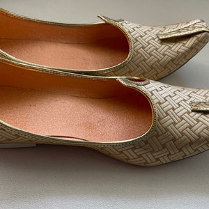 May include: A pair of gold-colored woven flat shoes with pointed toes. The shoes have a woven pattern and a pointed toe.