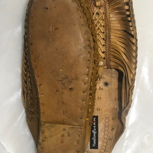 May include: A pair of brown leather sandals with a woven design. The sandals have a label that reads "handicrafts n me".