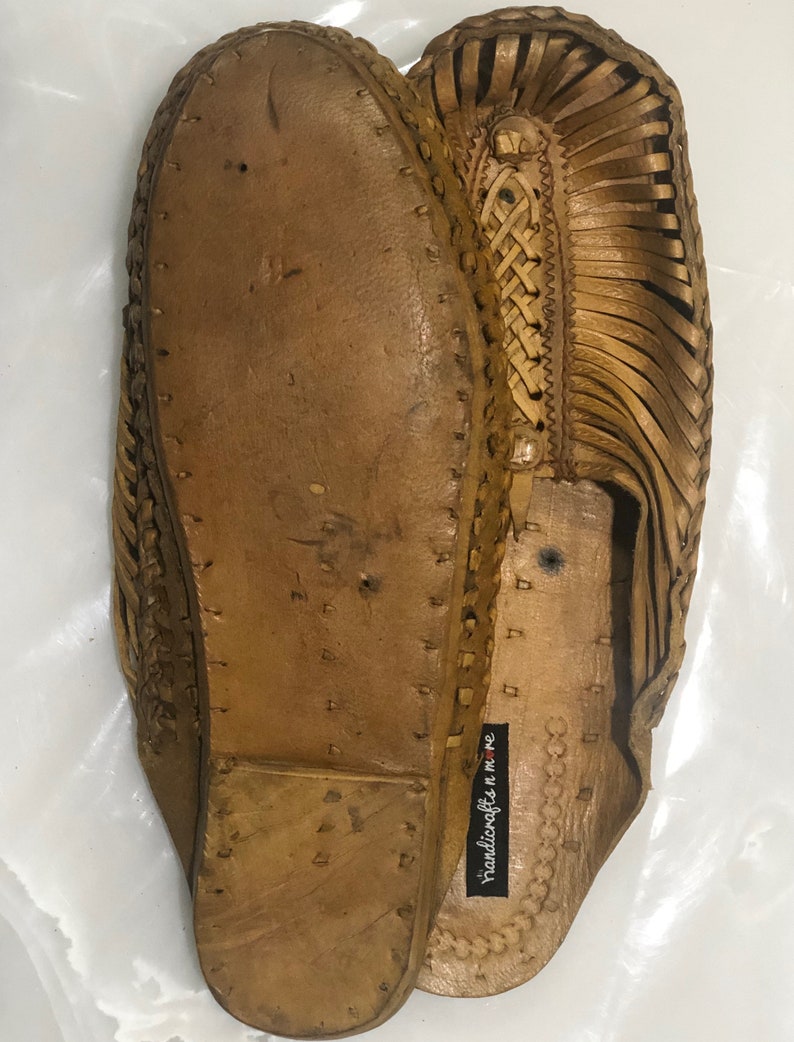 May include: A pair of brown leather sandals with a woven design. The sandals have a label that reads "handicrafts n me".