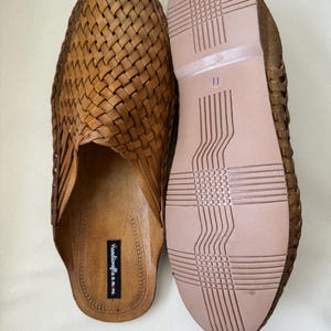 May include: A pair of brown leather woven slip-on shoes. The shoes have a woven upper design and a light brown sole. The sole of one shoe is visible, showing a size 11 marking. The shoes are handmade.