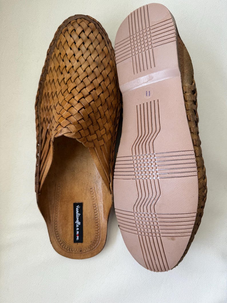 May include: A pair of brown leather woven slip-on shoes. The shoes have a woven upper design and a light brown sole. The sole of one shoe is visible, showing a size 11 marking. The shoes are handmade.