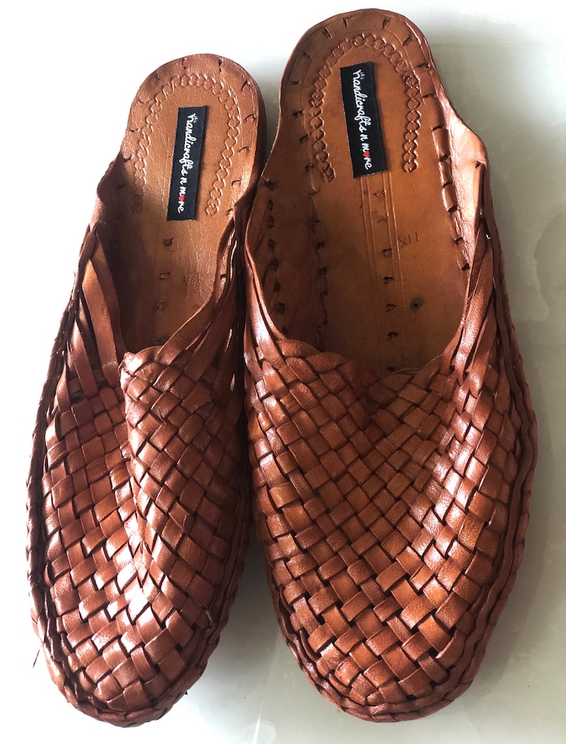 May include: A pair of brown leather woven slippers with a black label that reads "Handicrafts n more".