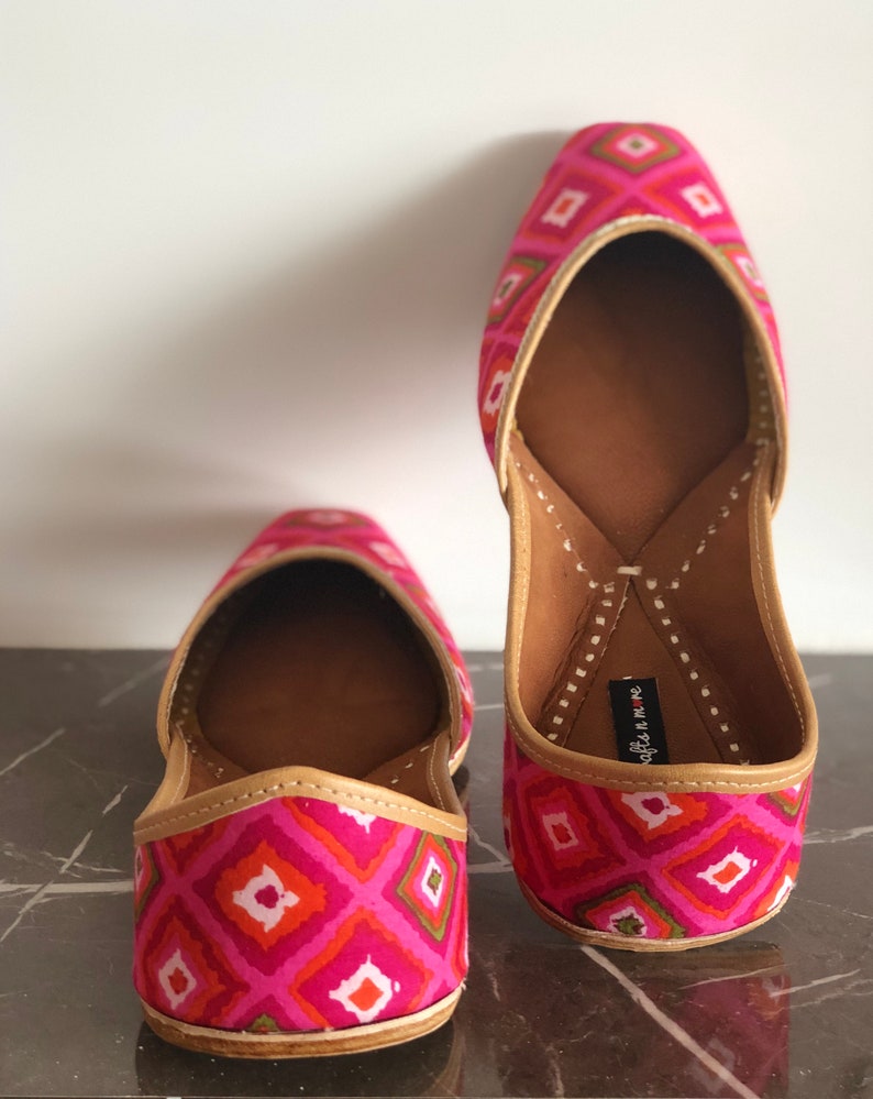 May include: A pair of pink and green patterned flat shoes with a pointed toe and a decorative stitch detail. The shoes have a brown leather insole and a gold trim.
