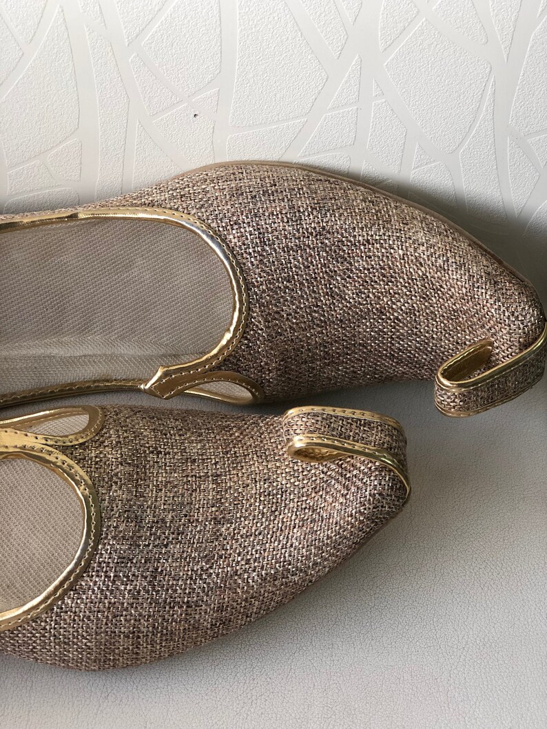 K&ouml;nnte beinhalten: Ein Paar braune und goldene Schuhe mit spitzer Zehenpartie und dekorativem goldenen Besatz. Die Schuhe sind aus einem gewebten Stoff.