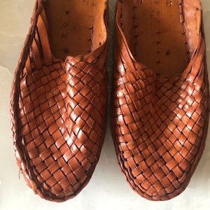 May include: A pair of brown leather woven slippers. The slippers have a woven pattern and are made of a soft, supple leather.