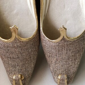 K&ouml;nnte beinhalten: Ein Paar braune und goldene spitze Schuhe mit einem strukturierten Obermaterial aus Stoff. Die Schuhe haben einen goldenen Besatz um die &Ouml;ffnung und einen goldenen Akzent an der Spitze.