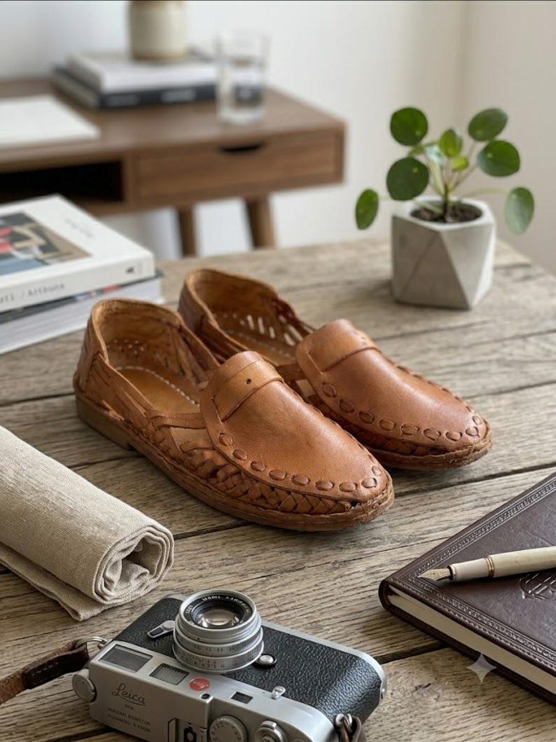 May include: A pair of tan leather loafers featuring a woven design across the vamp and sides, with a rounded toe, a low heel, and decorative stitching along the edges of the upper. The shoes have a slip-on construction with cut-out details.