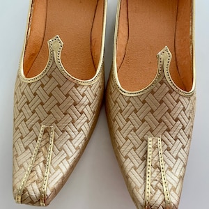 May include: A pair of gold-colored shoes with a woven pattern and pointed toes. The shoes have a decorative detail on the top.