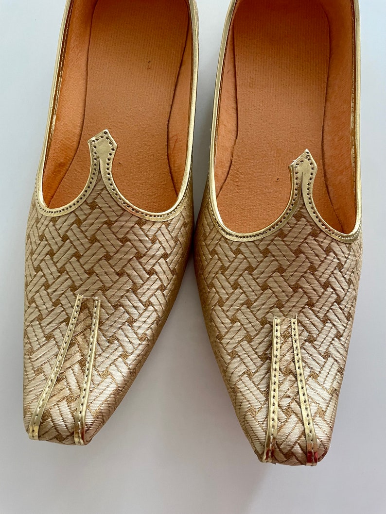 May include: A pair of gold-colored shoes with a woven pattern and pointed toes. The shoes have a decorative detail on the top.