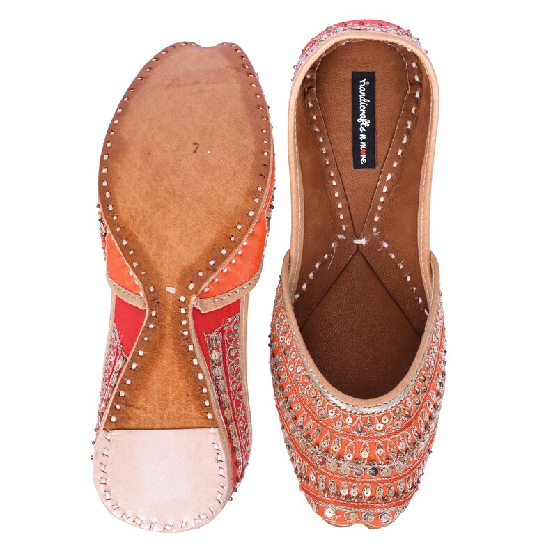 May include: A pair of orange and red embroidered flat shoes with gold embellishments. The shoes have a leather sole and are decorated with sequins and beads. The text "Handicrafts in me" is visible on the inside of one shoe.