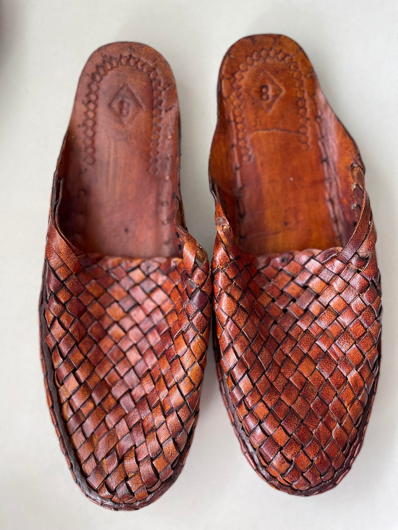 May include: A pair of brown leather woven slippers. The slippers have a woven pattern and a pointed toe.