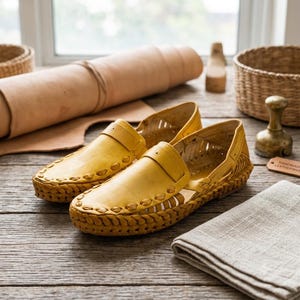May include: A pair of yellow leather loafers featuring a woven design along the sides and toe box, with a slip-on style and cut-out details. The shoes have a thick braided leather trim around the base and a smooth leather upper construction.