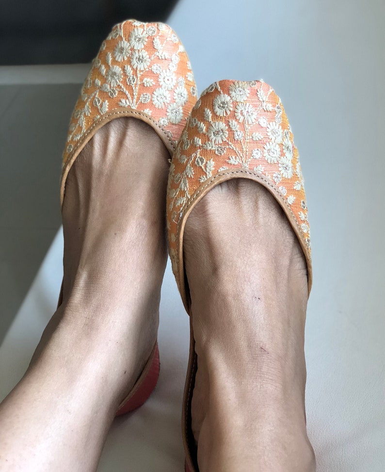 May include: A pair of orange and white embroidered flat shoes with a pointed toe.