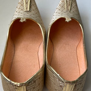 May include: A pair of gold-colored woven flat shoes with a pointed toe. The shoes have a woven pattern and a gold trim.