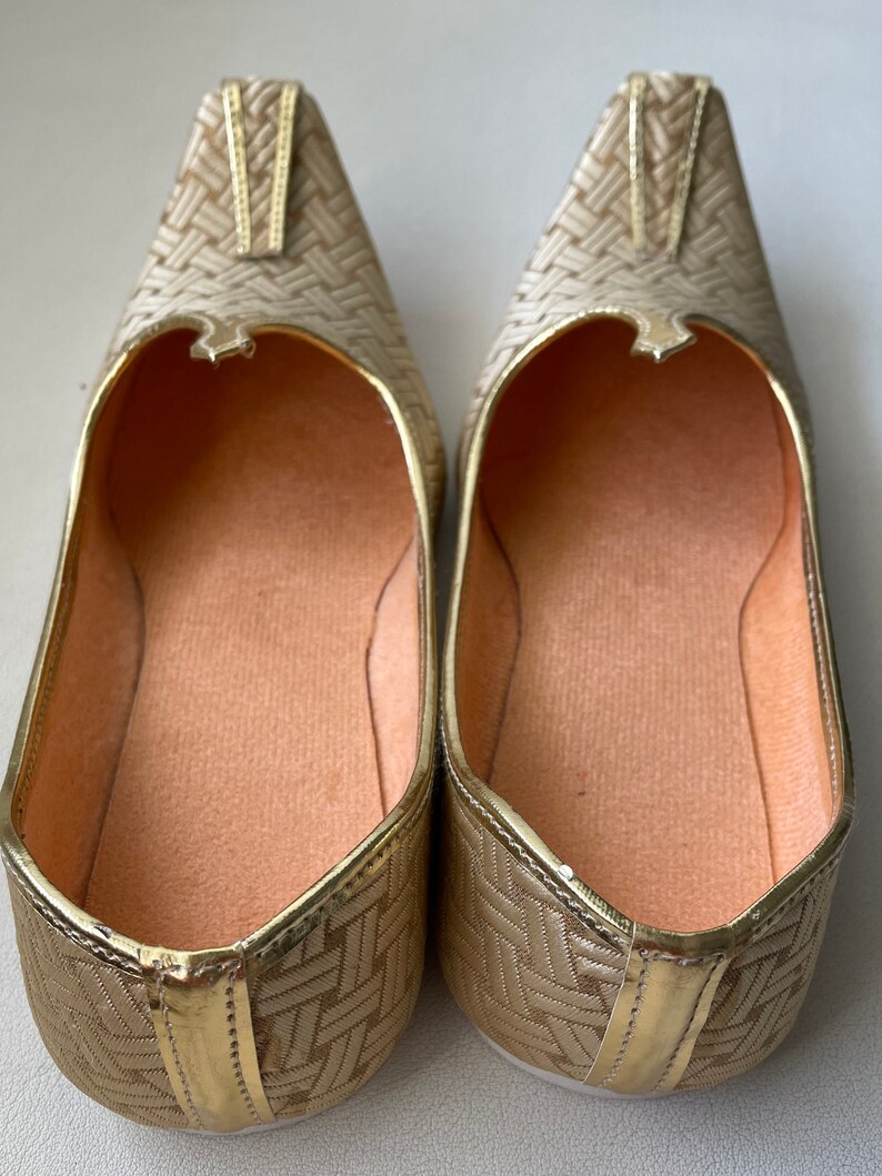 May include: A pair of gold-colored woven flat shoes with a pointed toe. The shoes have a woven pattern and a gold trim.