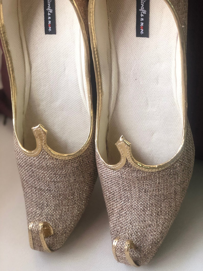 K&ouml;nnte beinhalten: Ein Paar goldene, glitzernde flache Schuhe mit spitzer Zehenpartie und einem kleinen goldenen Besatzdetail. Die Schuhe haben eine wei&szlig;e Innensohle mit dem aufgedruckten Text "nicrafts n more".
