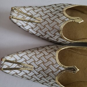 May include: A pair of gold and white patterned shoes with pointed toes and a decorative strap across the top.