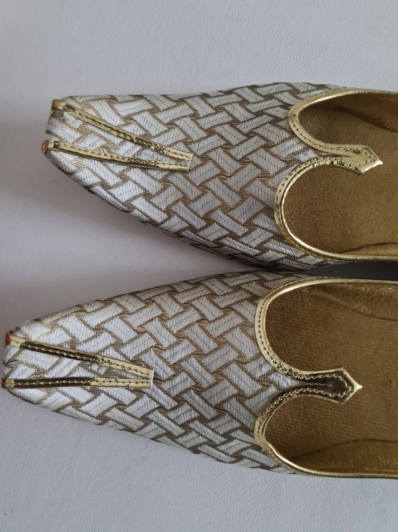 May include: A pair of gold and white patterned shoes with pointed toes and a decorative strap across the top.