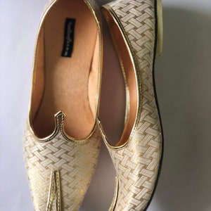 May include: A pair of gold and white woven pointed-toe flat shoes. The shoes have a woven pattern and a pointed toe.