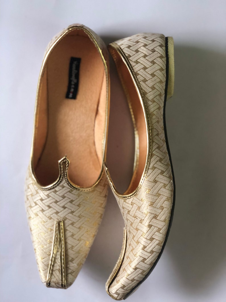 May include: A pair of gold and white woven pointed-toe flat shoes. The shoes have a woven pattern and a pointed toe.