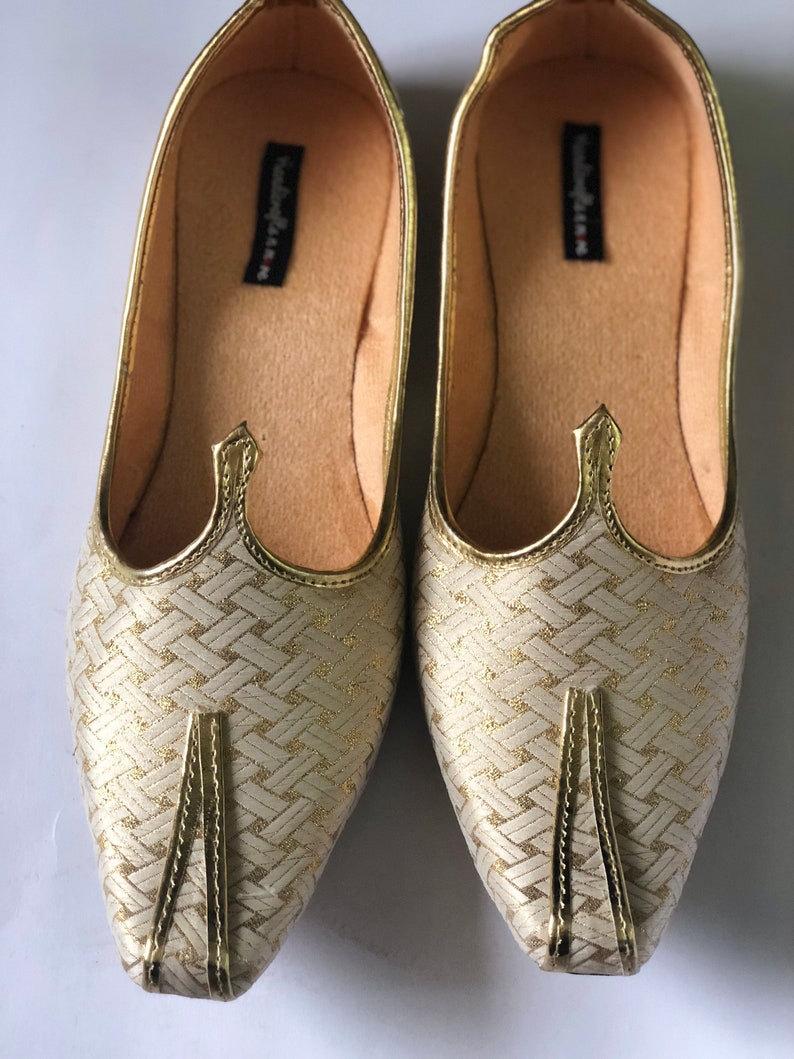 May include: A pair of gold and white woven flat shoes with gold trim. The shoes have a pointed toe and a flat sole.