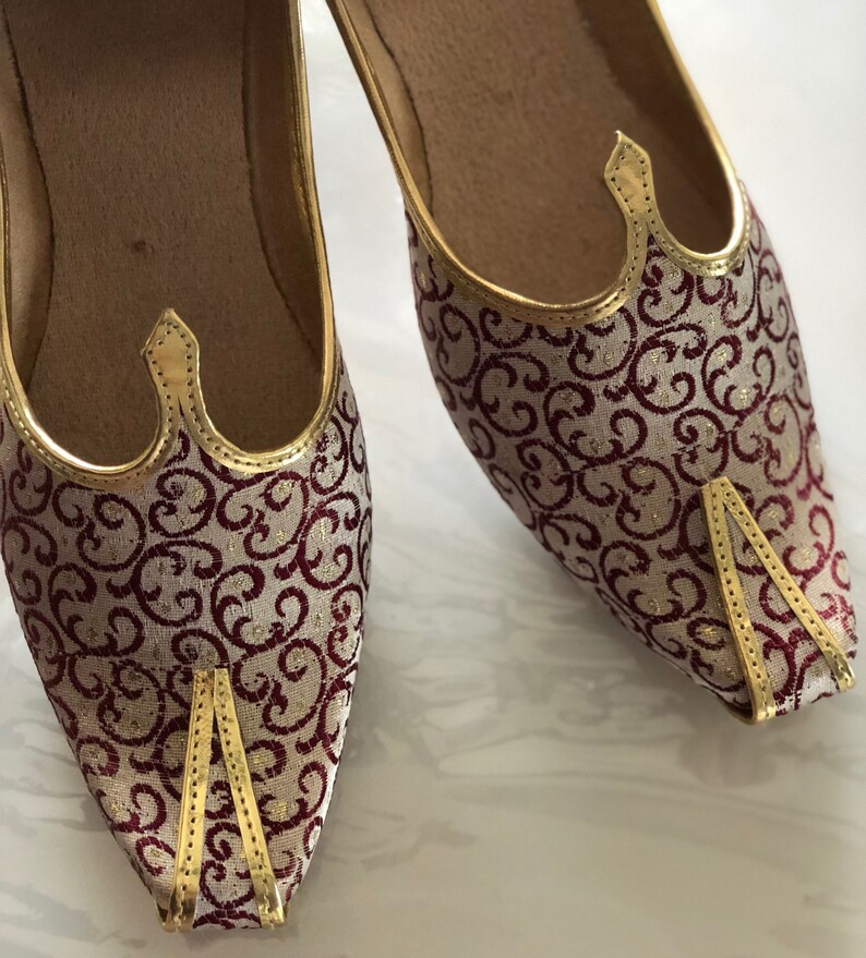 May include: A pair of gold and burgundy patterned shoes with pointed toes and gold trim. The shoes have a traditional design.