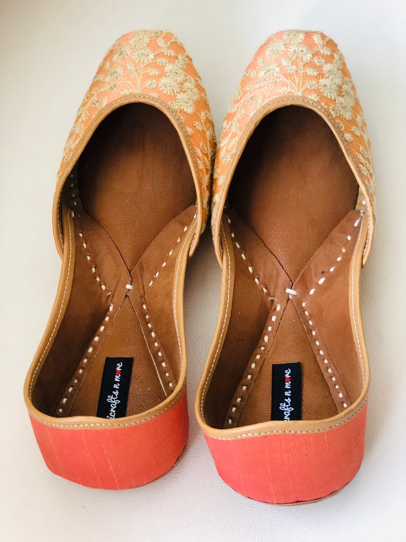 May include: A pair of peach-coloured embroidered flat shoes with a red sole and the text "juxtapose n me" on the inside of each shoe.