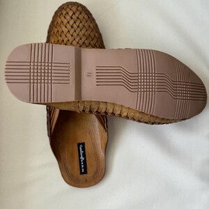 May include: A pair of brown woven leather sandals. The sandals have a textured sole and a woven upper design. The sole is a light brown color, and the upper is a darker brown. The sandals are designed for casual wear.