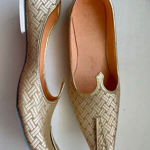 May include: A pair of gold-colored, pointed-toe shoes with a woven pattern. The shoes have a flat sole and a pointed toe.