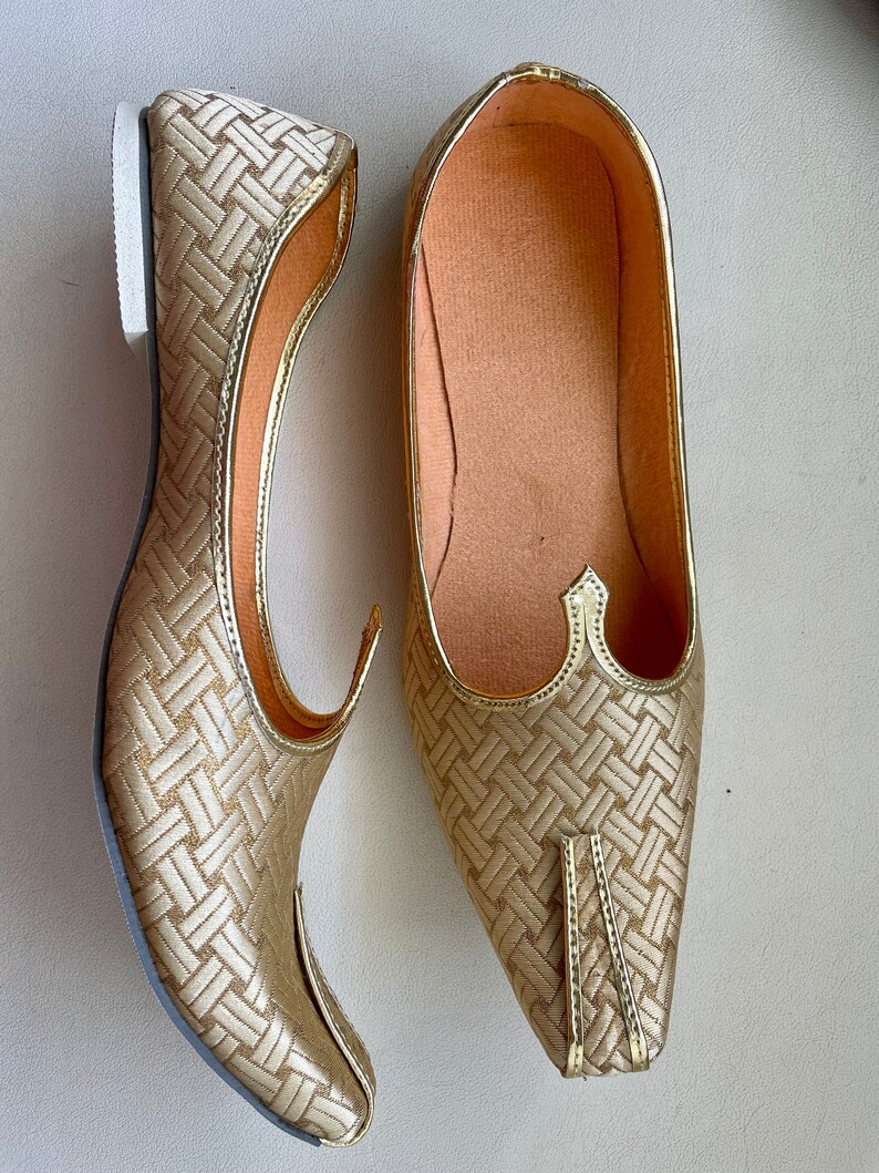May include: A pair of gold-colored, pointed-toe shoes with a woven pattern. The shoes have a flat sole and a pointed toe.