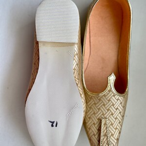 May include: A pair of gold woven fabric shoes with pointed toes. The shoes have a white leather sole with a size 11 written on the bottom.