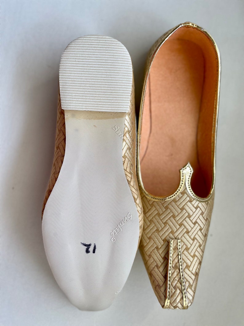 May include: A pair of gold woven fabric shoes with pointed toes. The shoes have a white leather sole with a size 11 written on the bottom.