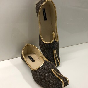 May include: A pair of brown woven fabric shoes with gold trim. The shoes have a pointed toe and a flat sole. The brand name "handicrafts" is printed on the inside of the shoes.