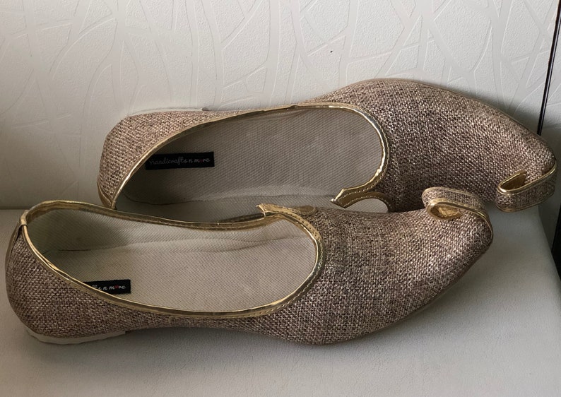 K&ouml;nnte beinhalten: Ein Paar goldene und braune Stoffschuhe mit spitzer Zehenpartie und einem dekorativen Detail an der Oberseite. Die Schuhe haben einen goldenen Rand.