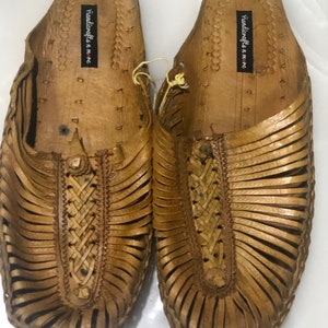 May include: A pair of brown leather sandals with a woven design. The sandals have a label that reads "Handicrafts in me".