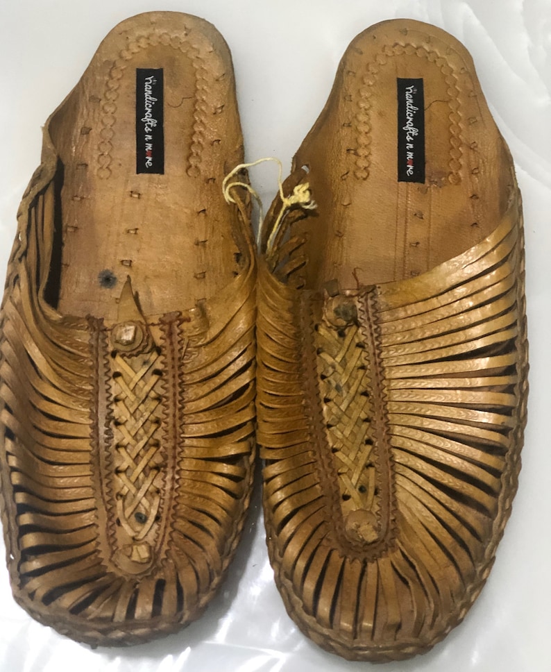 May include: A pair of brown leather sandals with a woven design. The sandals have a label that reads "Handicrafts in me".